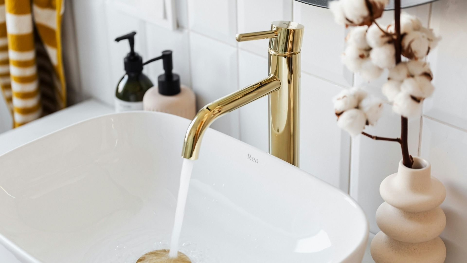 Modern bathroom sink with gold faucet, soap dispensers, and cotton flowers decor