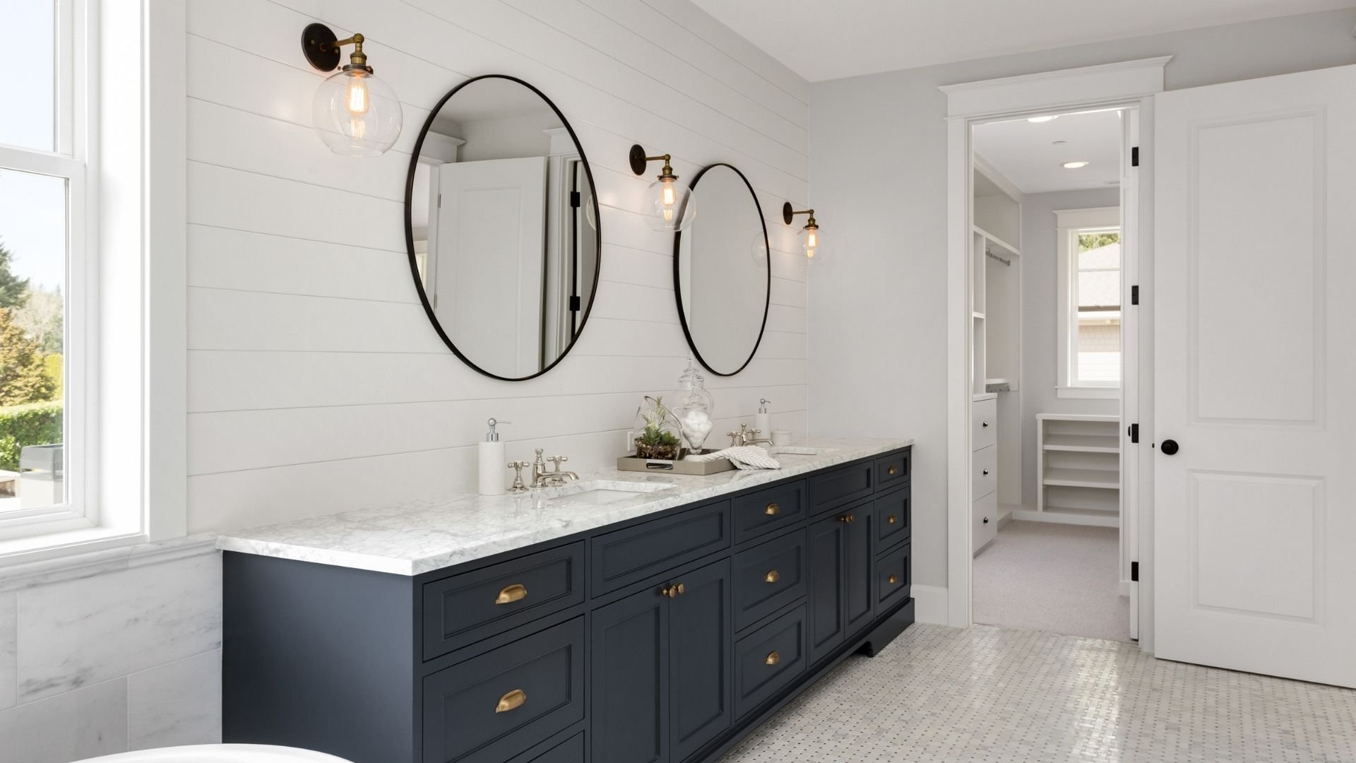 Modern bathroom with dual vanity, black cabinets, marble countertop, round mirrors, and pendant lights