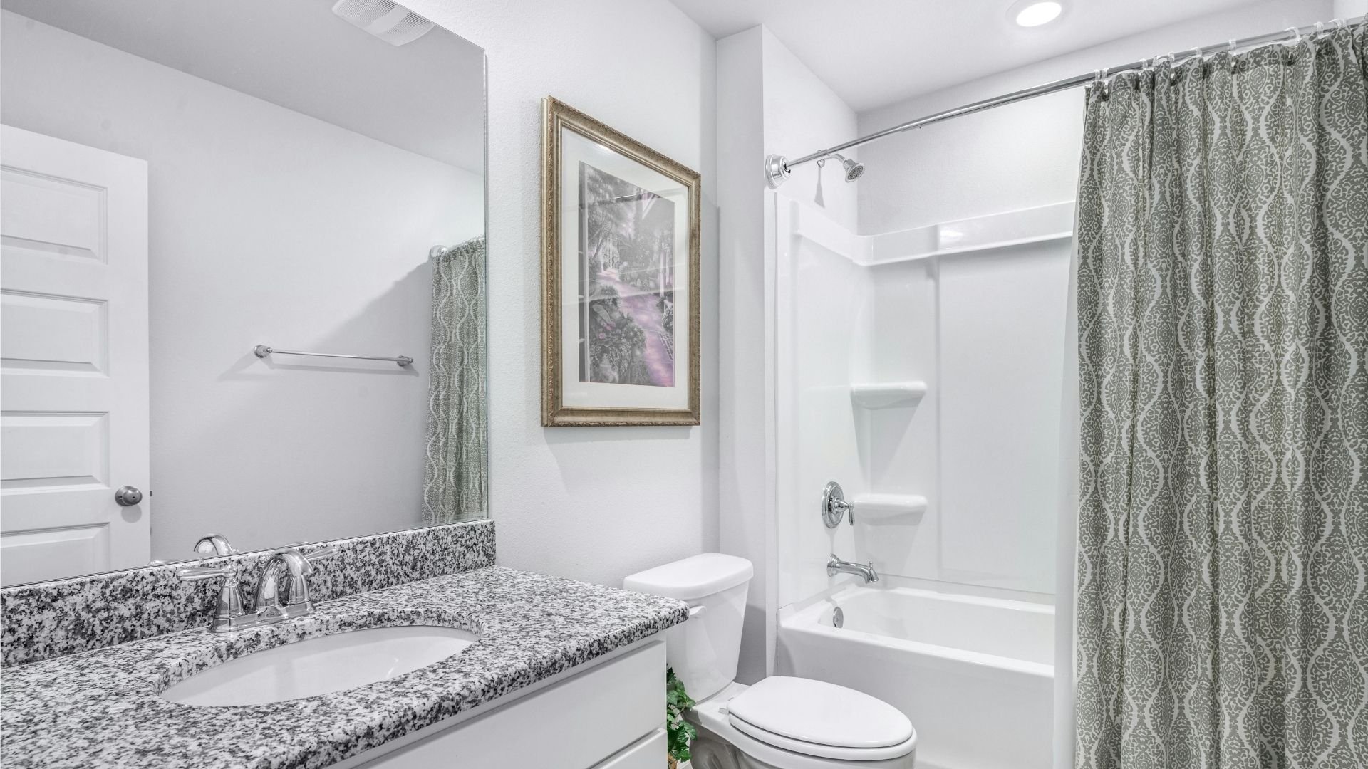 Modern bathroom with speckled granite countertop, framed artwork, shower, and green patterned curtain.